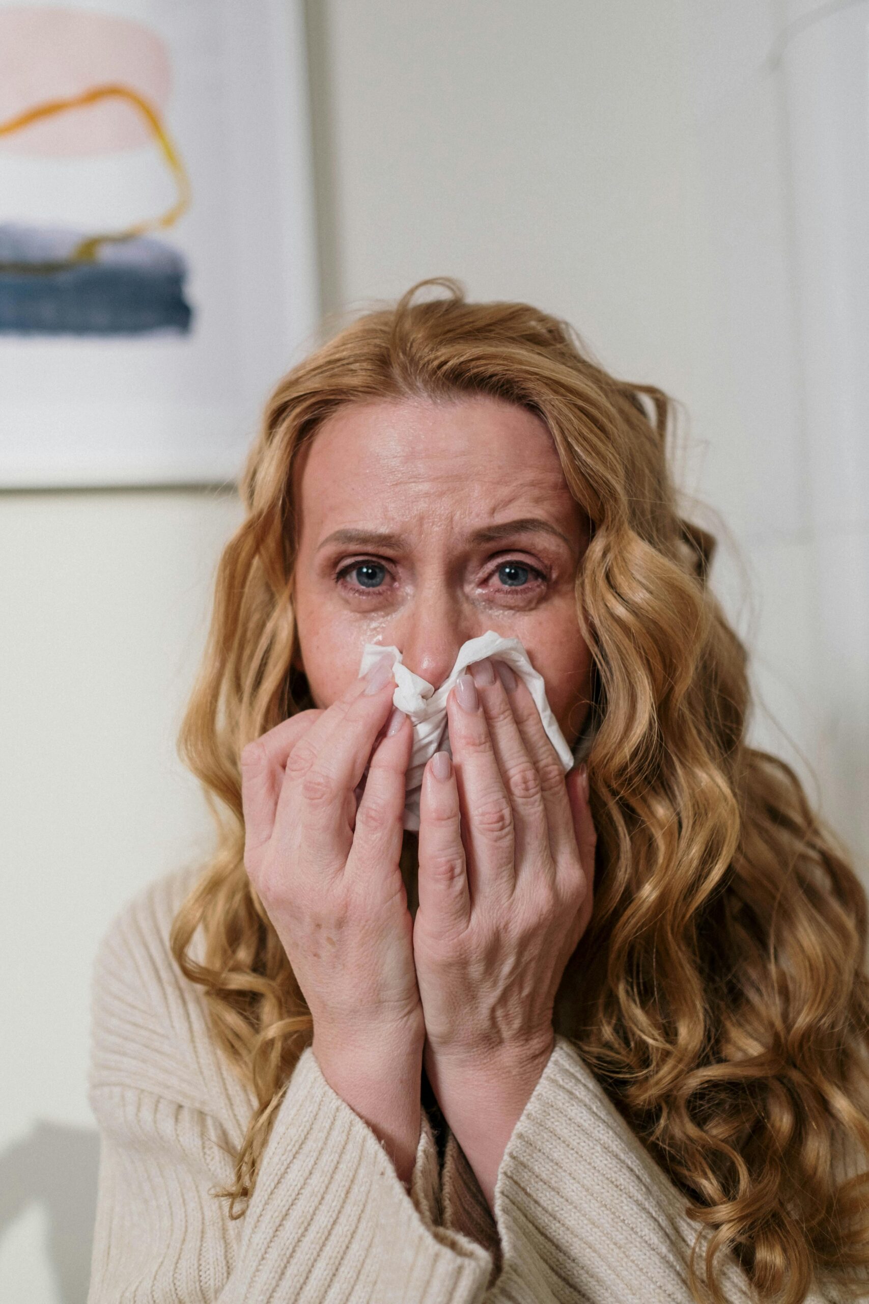 Woman with swollen eyes from allergies blowing her nose with a tissue